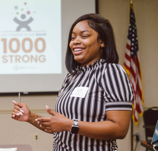 An African-American female SCI employee wearing a striped shirt speaks at an event.