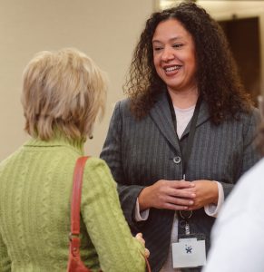 A smiling woman with long blond hair is wearing a white shirt with a black blazer.  This is a headshot of Kasey Bly, SCI's Program Navigator.