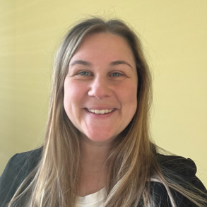 A smiling woman with long blond hair is wearing a white shirt with a black blazer.  This is a headshot of Kasey Bly, SCI's Program Navigator.