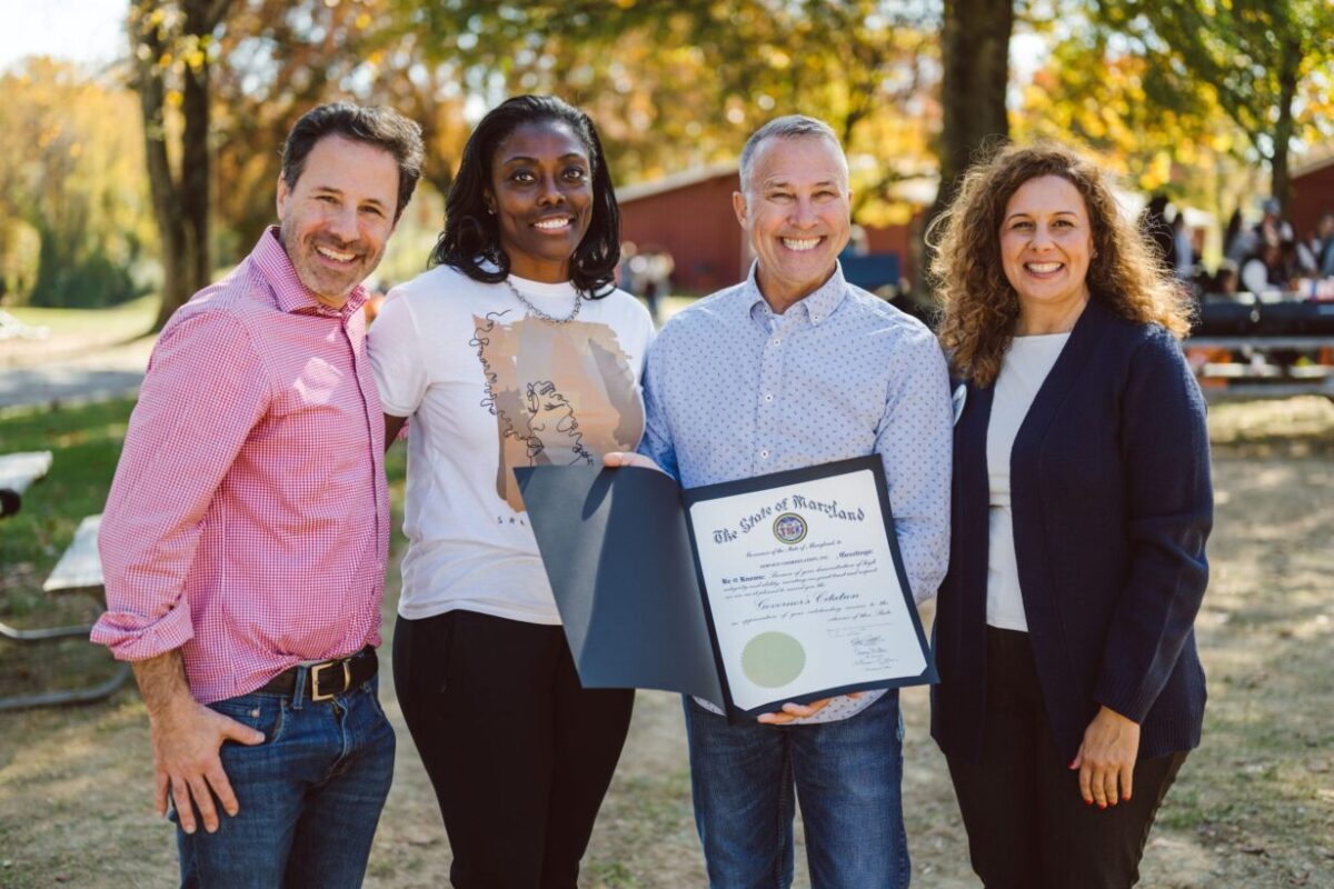 Four SCI leadership executives are standing next to each other, smiling and holding a document from the State of Maryland.