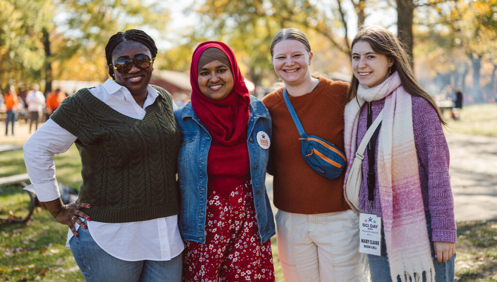 Four multicultural SCI employees smile and stand together at an event.