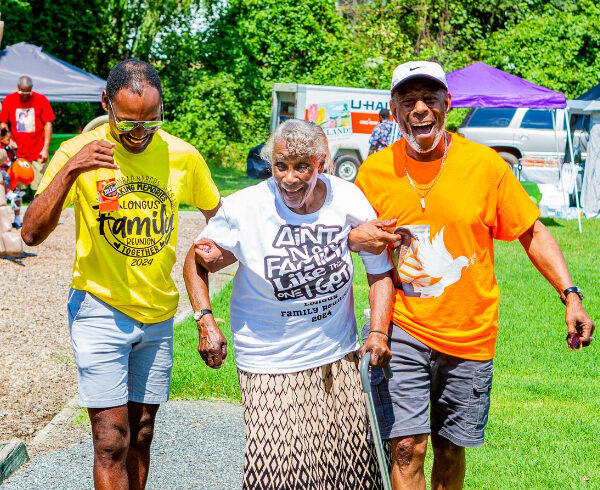 Elderly African American woman being escorted by 2 African American men along a path outside in a park