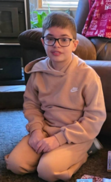 Young Boy in light colored Nike sweatsuit sitting on his feet in front of a couch