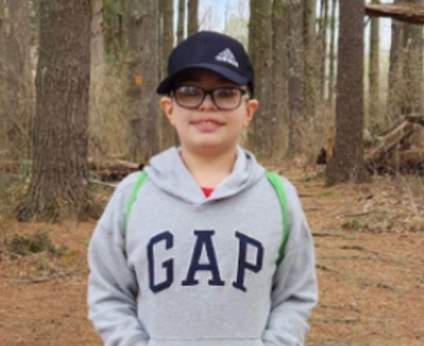 Young boy smiling in the woods with a baseball cap and wearing a grey gap sweatshirt